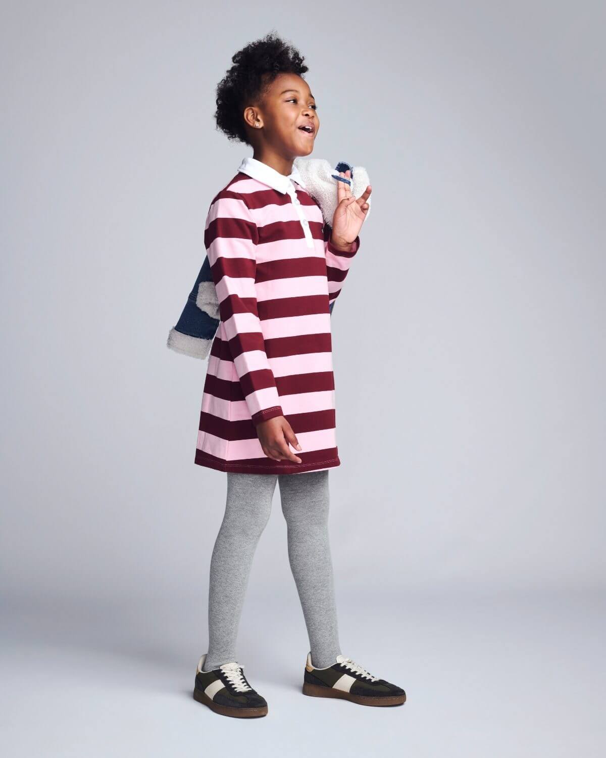 Child wearing a red and white striped dress with gray leggings on a plain background