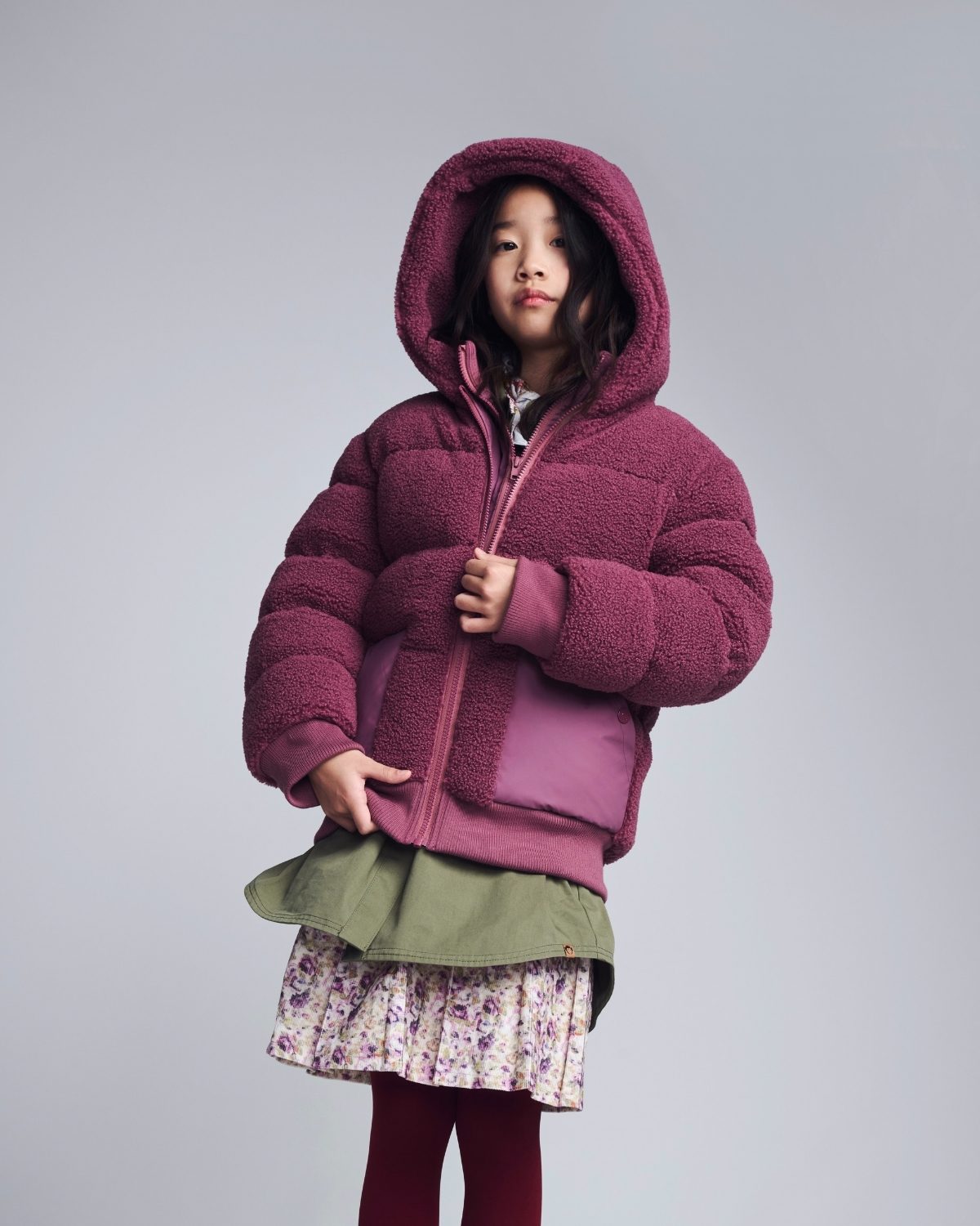 Child wearing a pink hooded jacket on a gray background