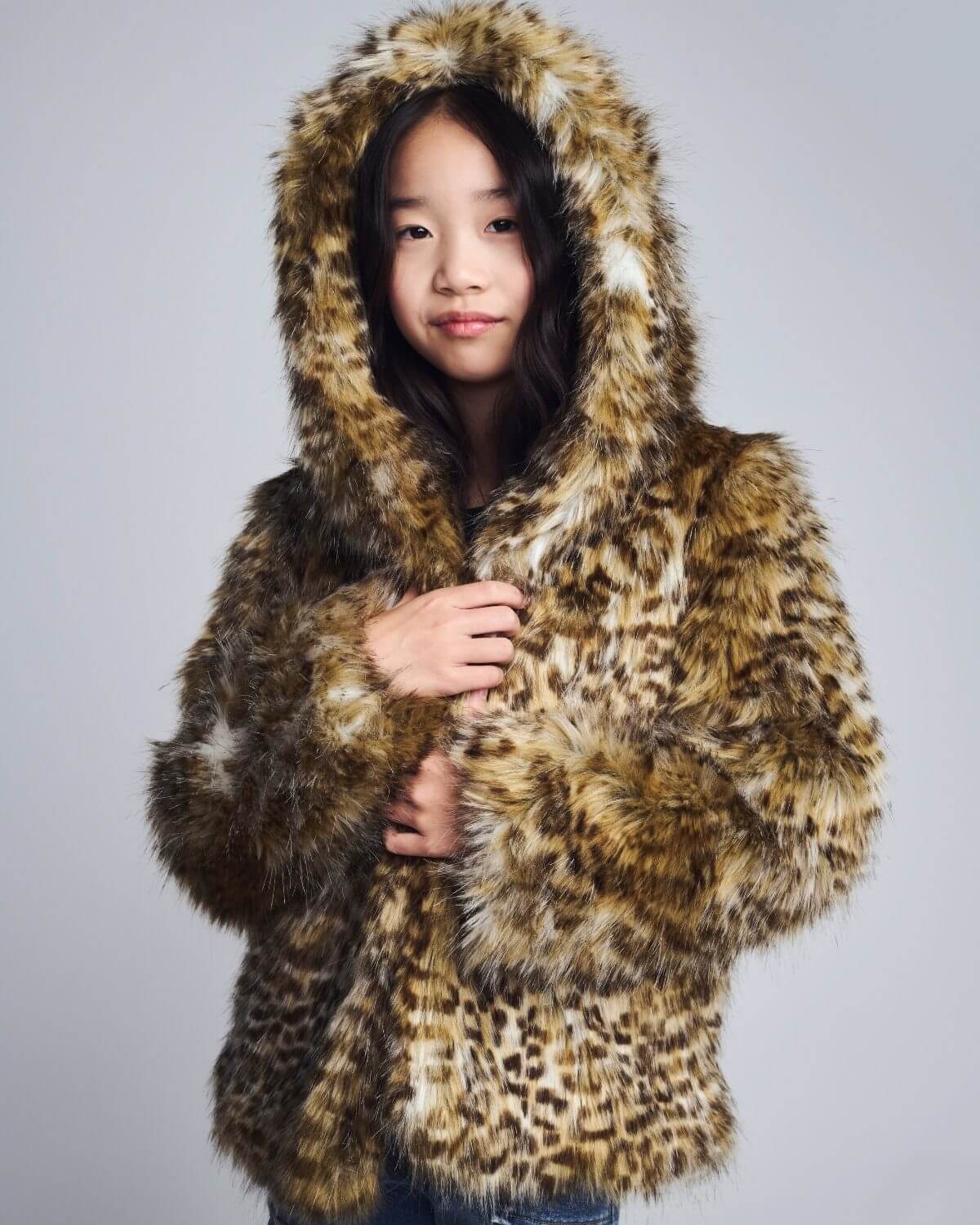 Girl wearing a leopard print fur coat against a plain background