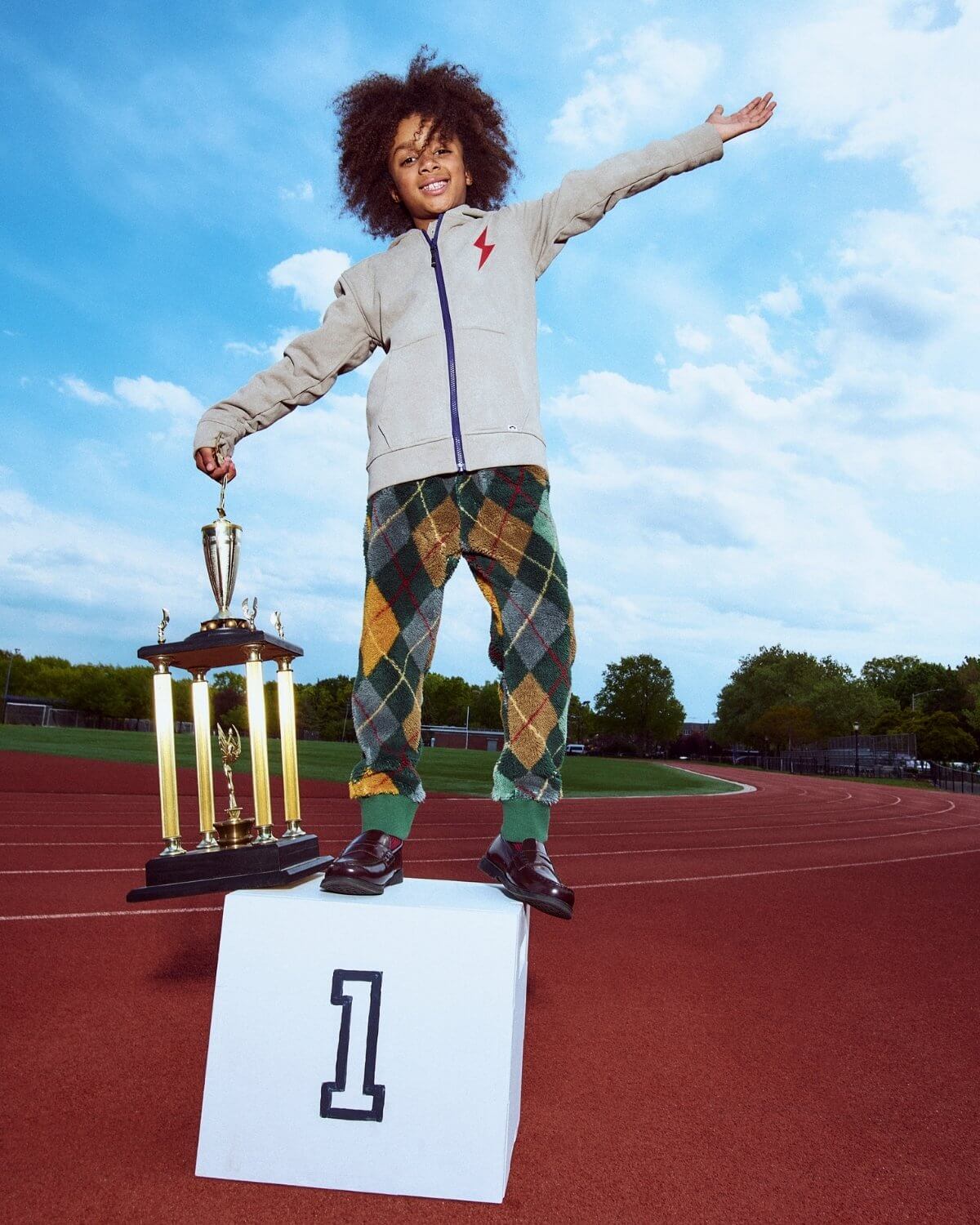 Child on a podium with a trophy, celebrating a win on a track field.