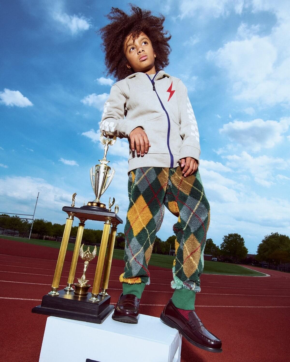 Child standing on a track holding a trophy with a blue sky background