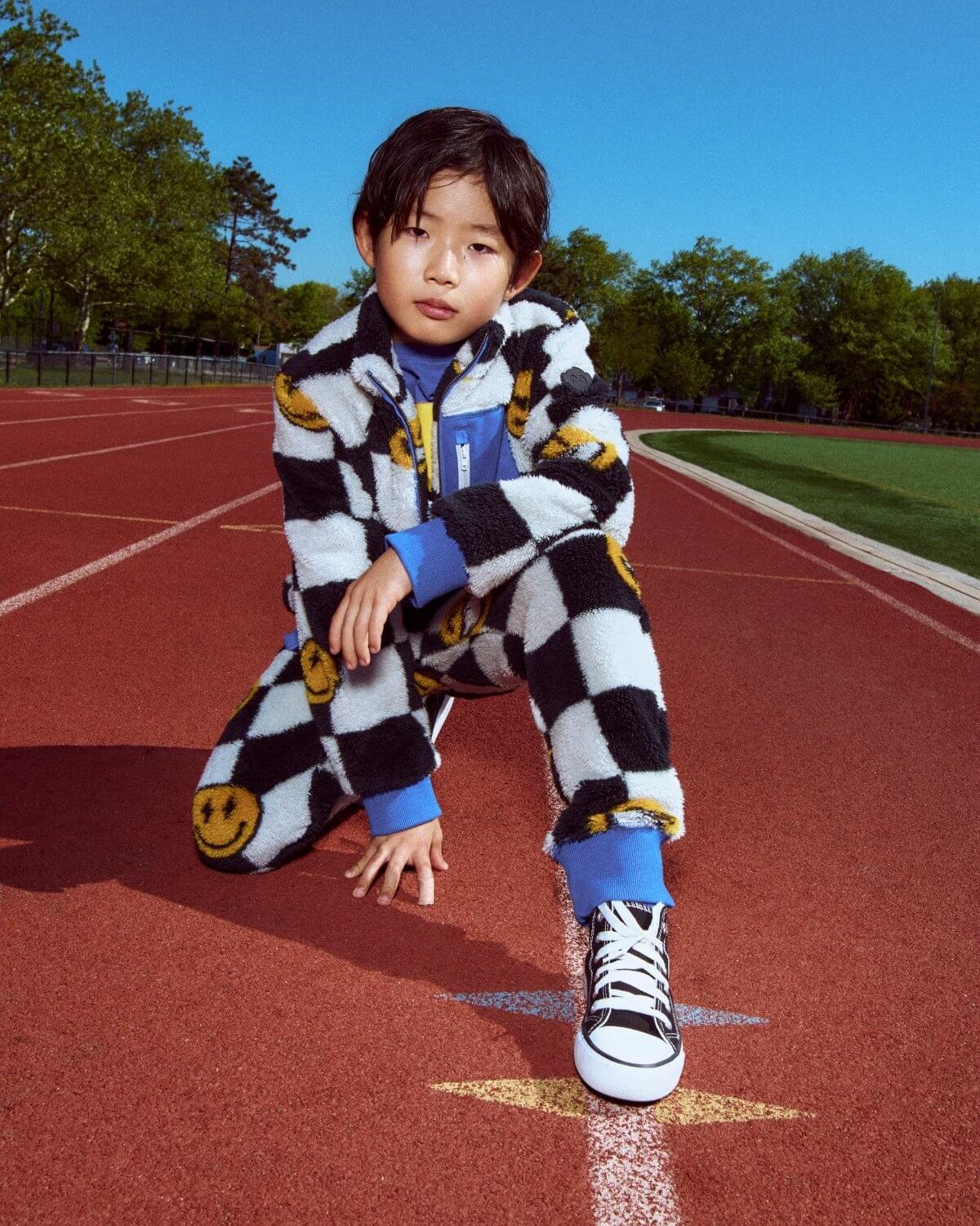 Child in a checkered outfit on a running track with trees in the background