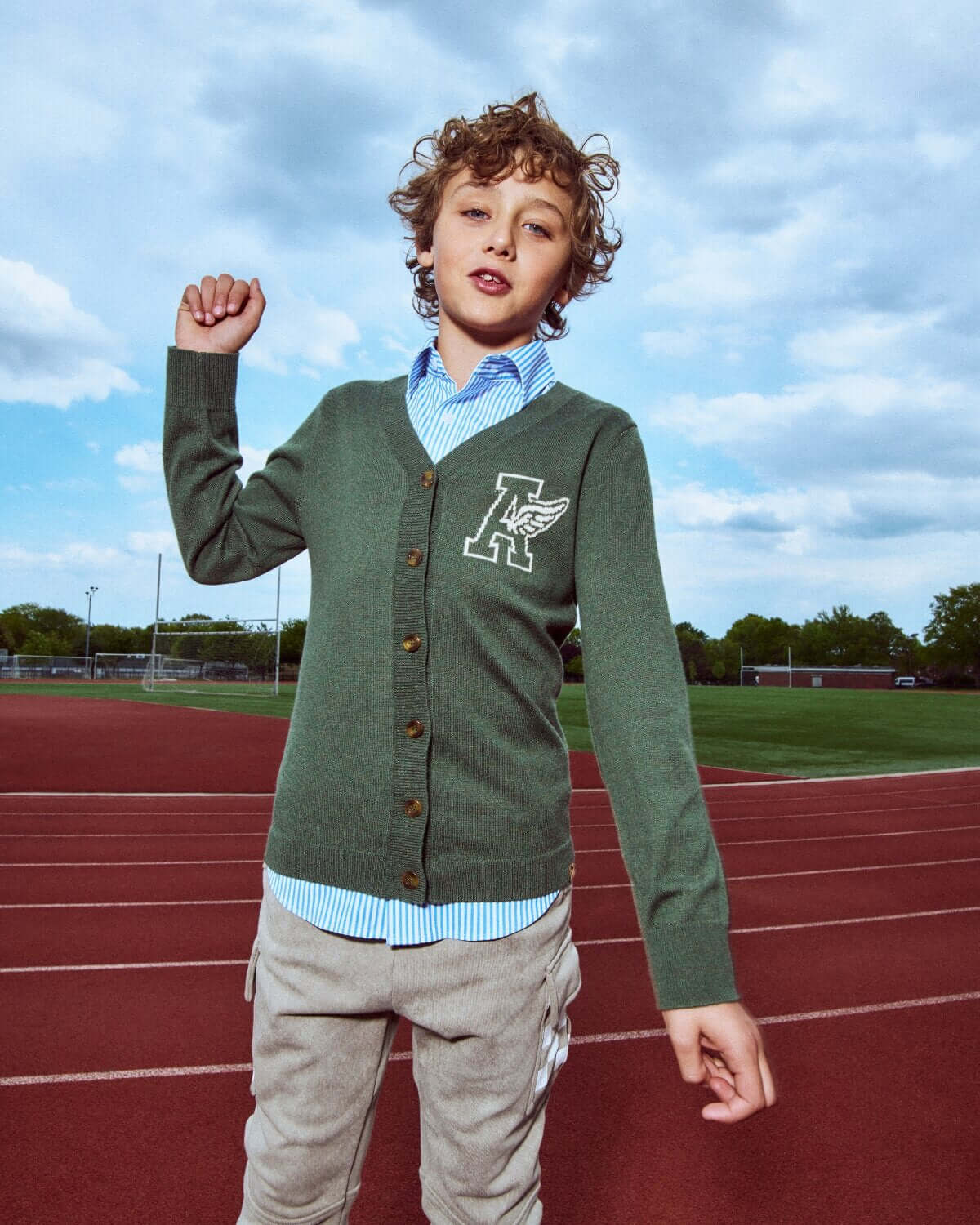 Child wearing a green cardigan with a logo on a track field