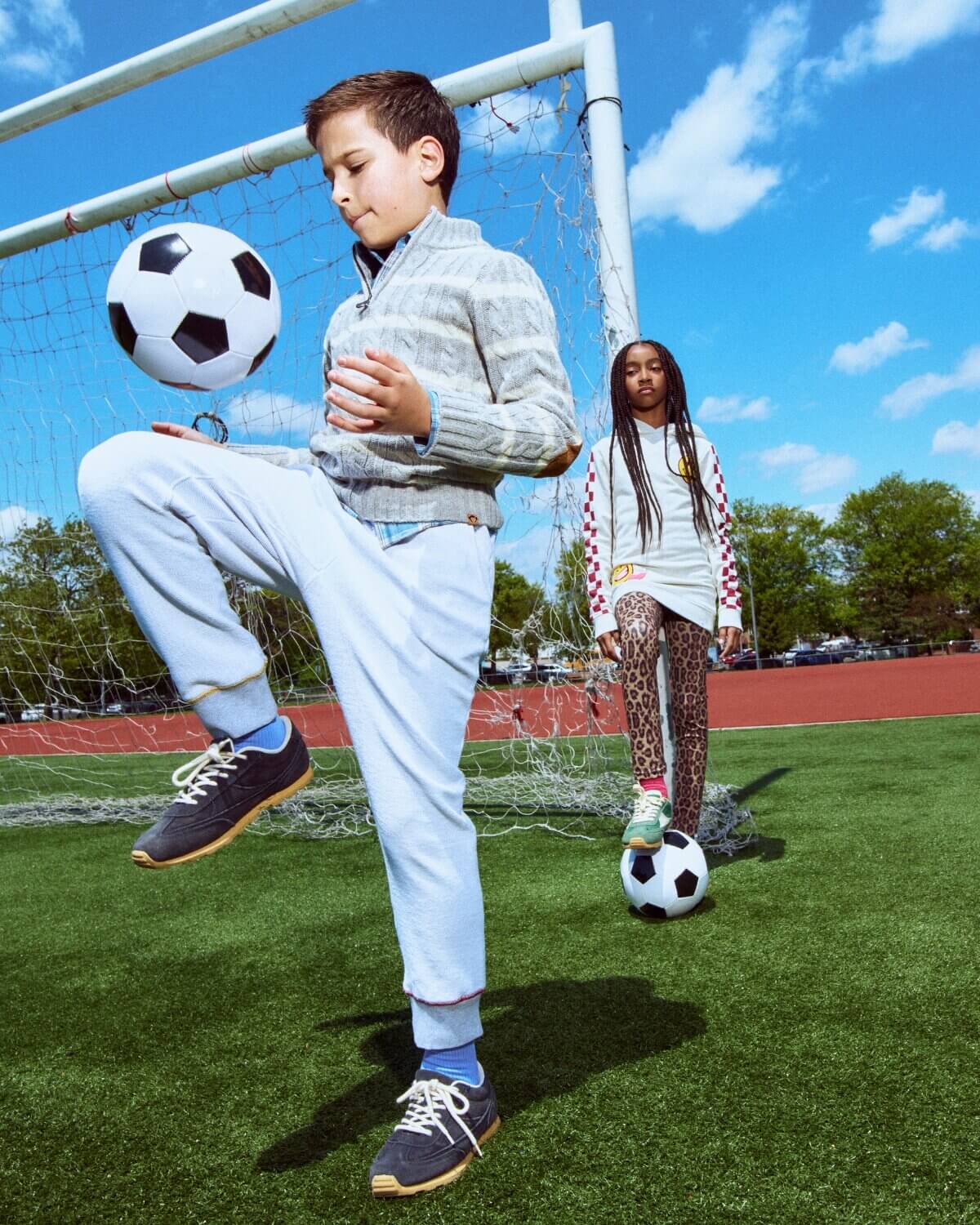 Two children playing soccer on a field with a clear blue sky.