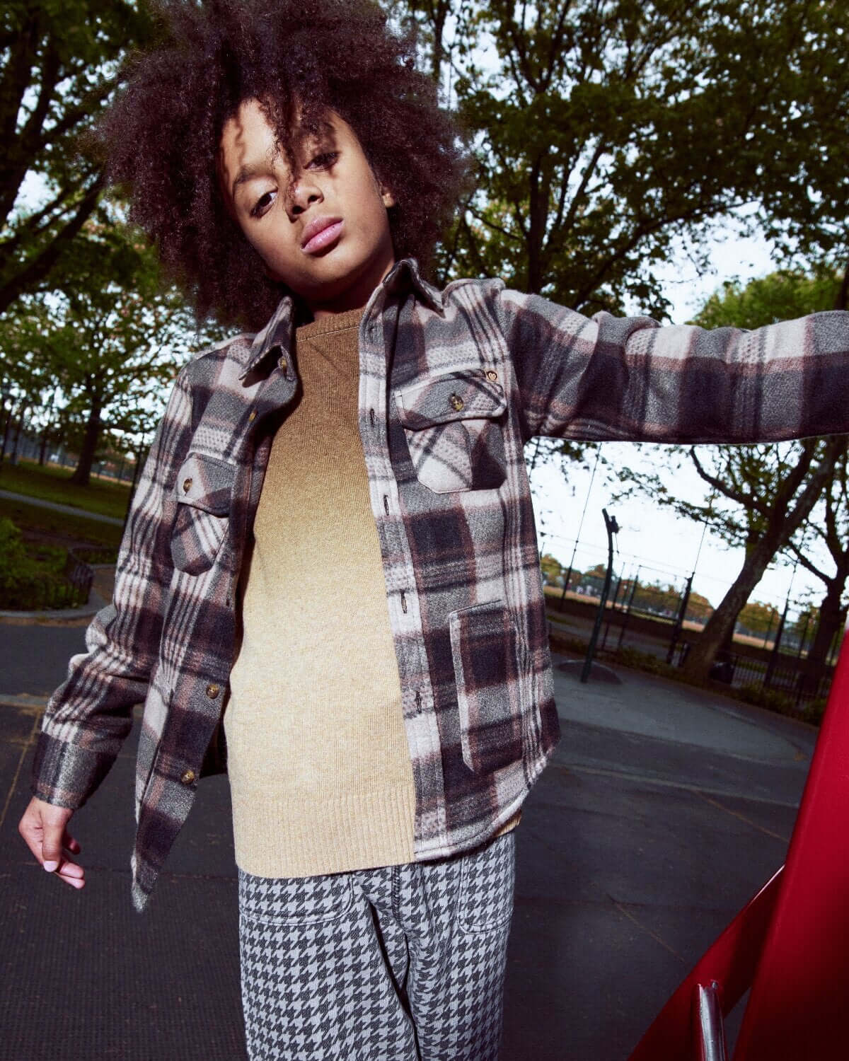 Person wearing a plaid shirt over a beige sweater with checkered pants outdoors.