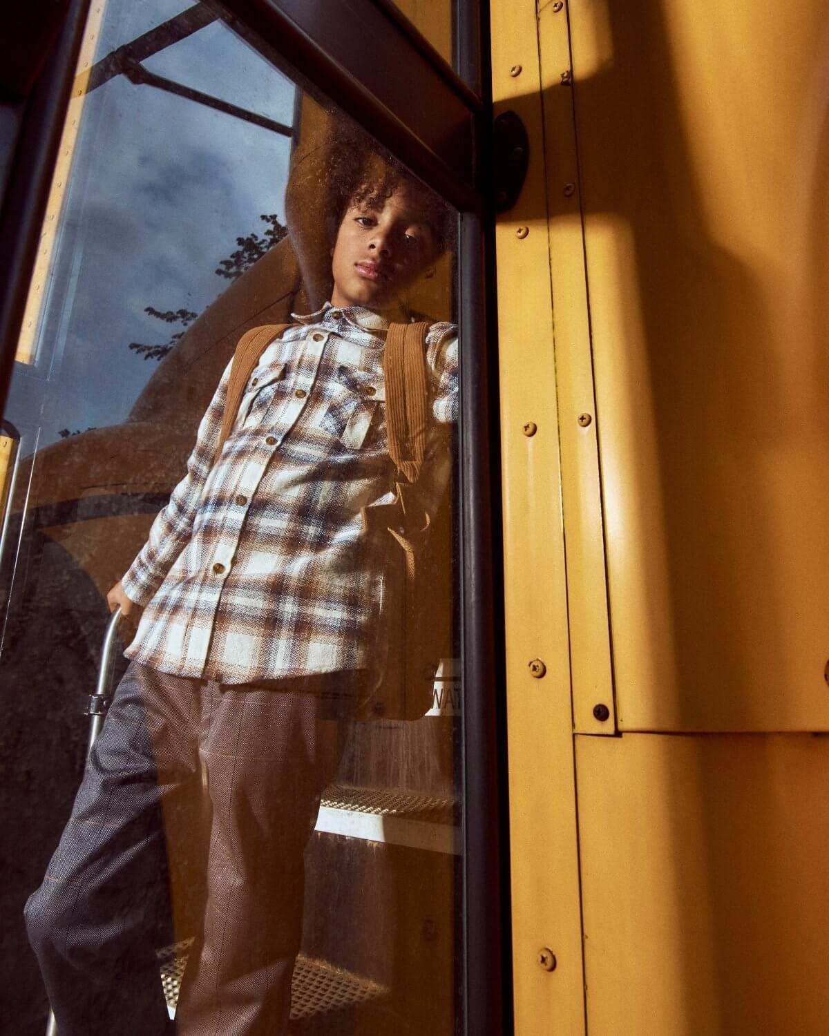 Person standing inside a yellow vehicle, wearing a plaid shirt and backpack.