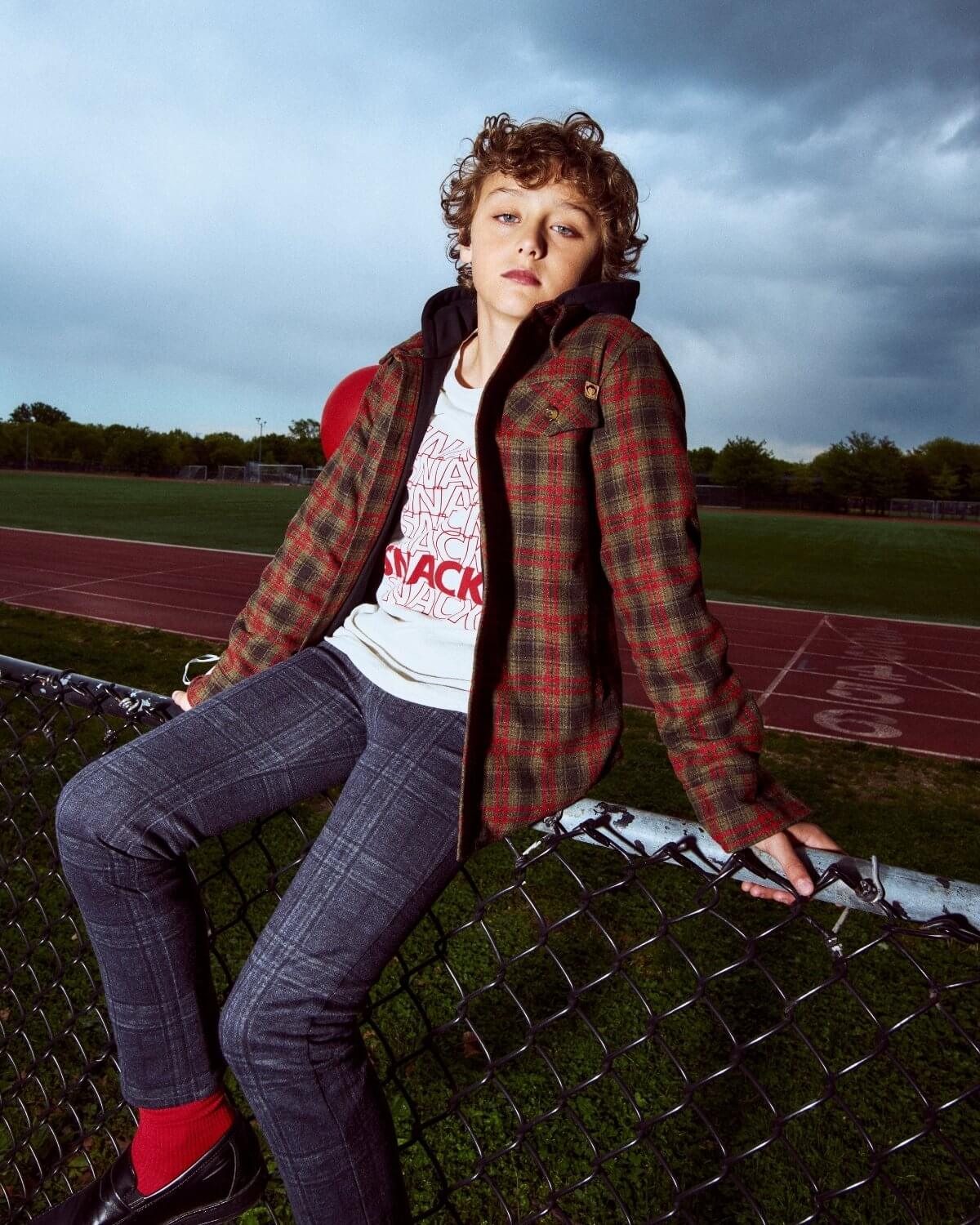 Person sitting on a chain-link fence with a track and field background