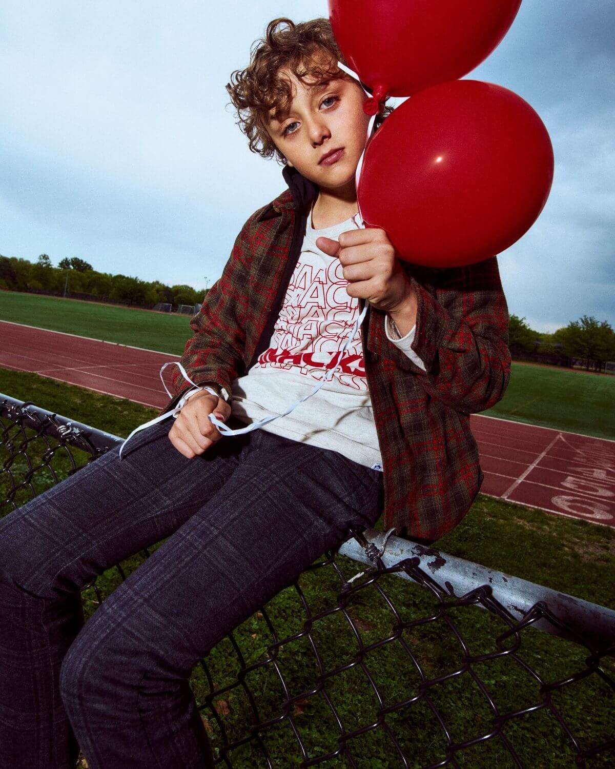 Child holding red balloons on a sports field