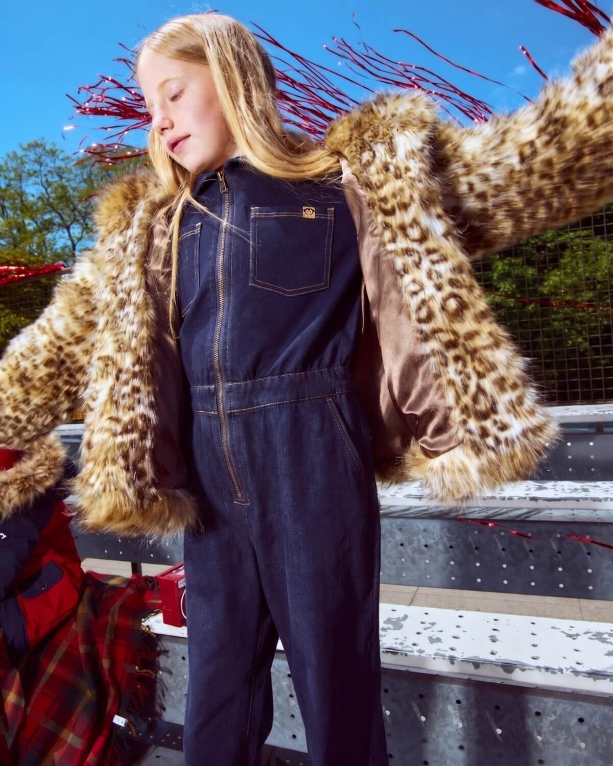 Person wearing a denim jumpsuit with a leopard print fur coat in an outdoor setting.
