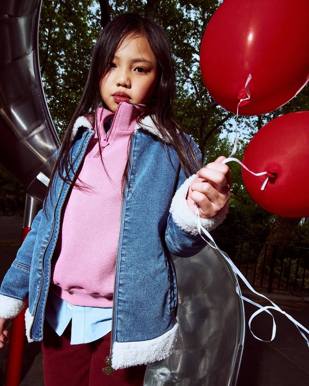 Child holding red balloons outdoors with trees in the background