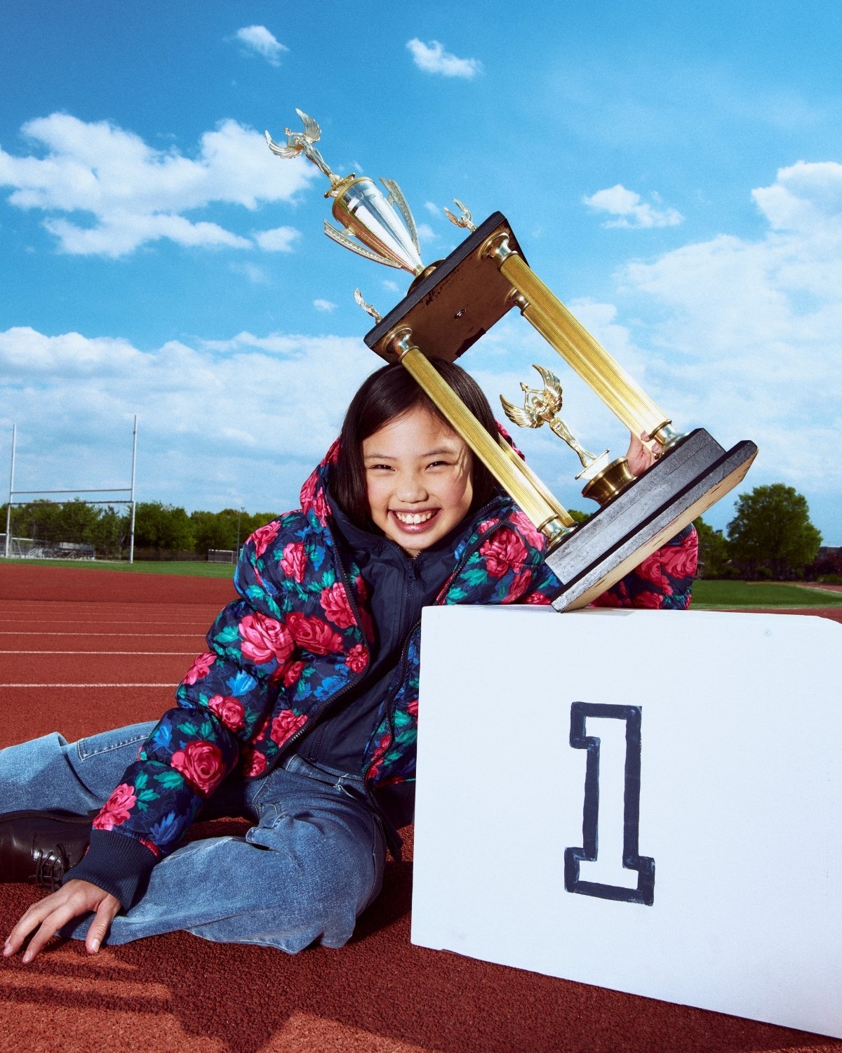Child with trophies on a track and field, smiling at the camera
