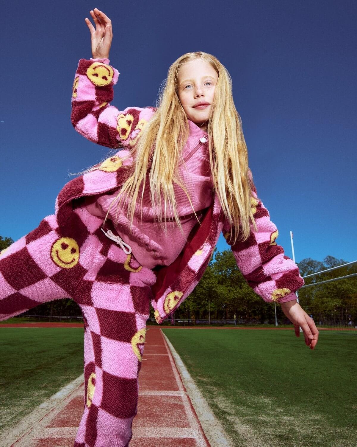 Person wearing a pink and maroon checkered outfit with smiley face patterns on a sports field.