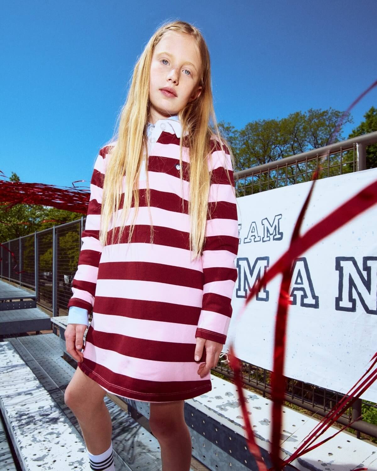 Young girl wearing a red and white striped dress standing outdoors with a clear blue sky.