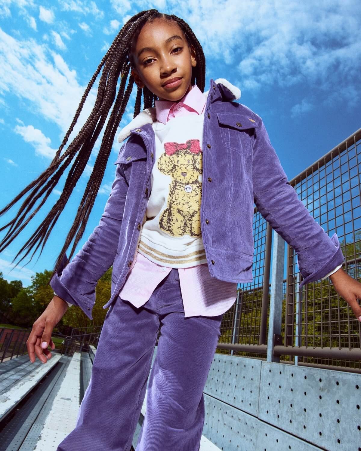 Young girl in a purple outfit standing on a bridge with a blue sky background