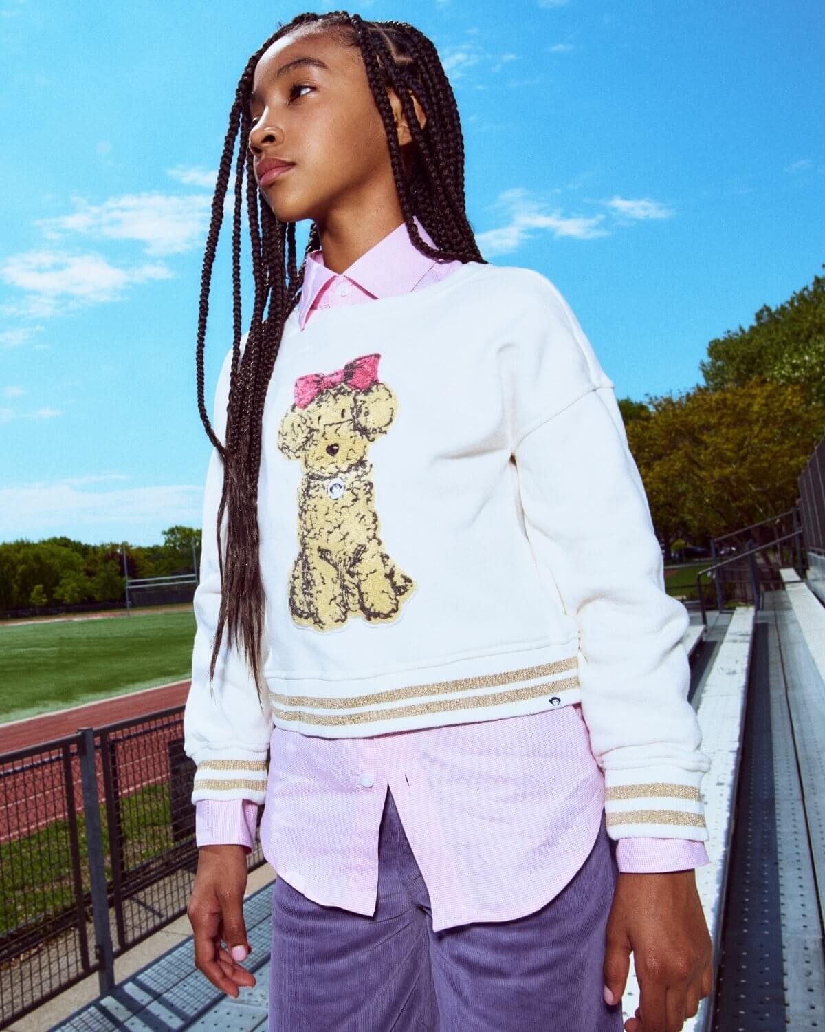 Person wearing a white sweater with a teddy bear design and a pink shirt, standing outdoors.