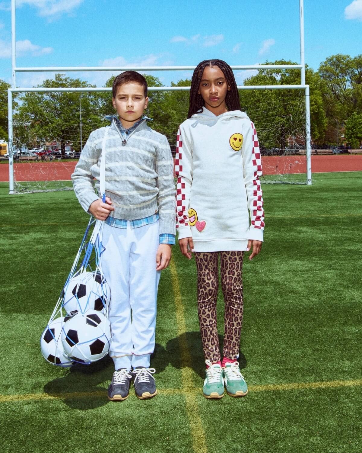 Two children standing on a soccer field with sports equipment
