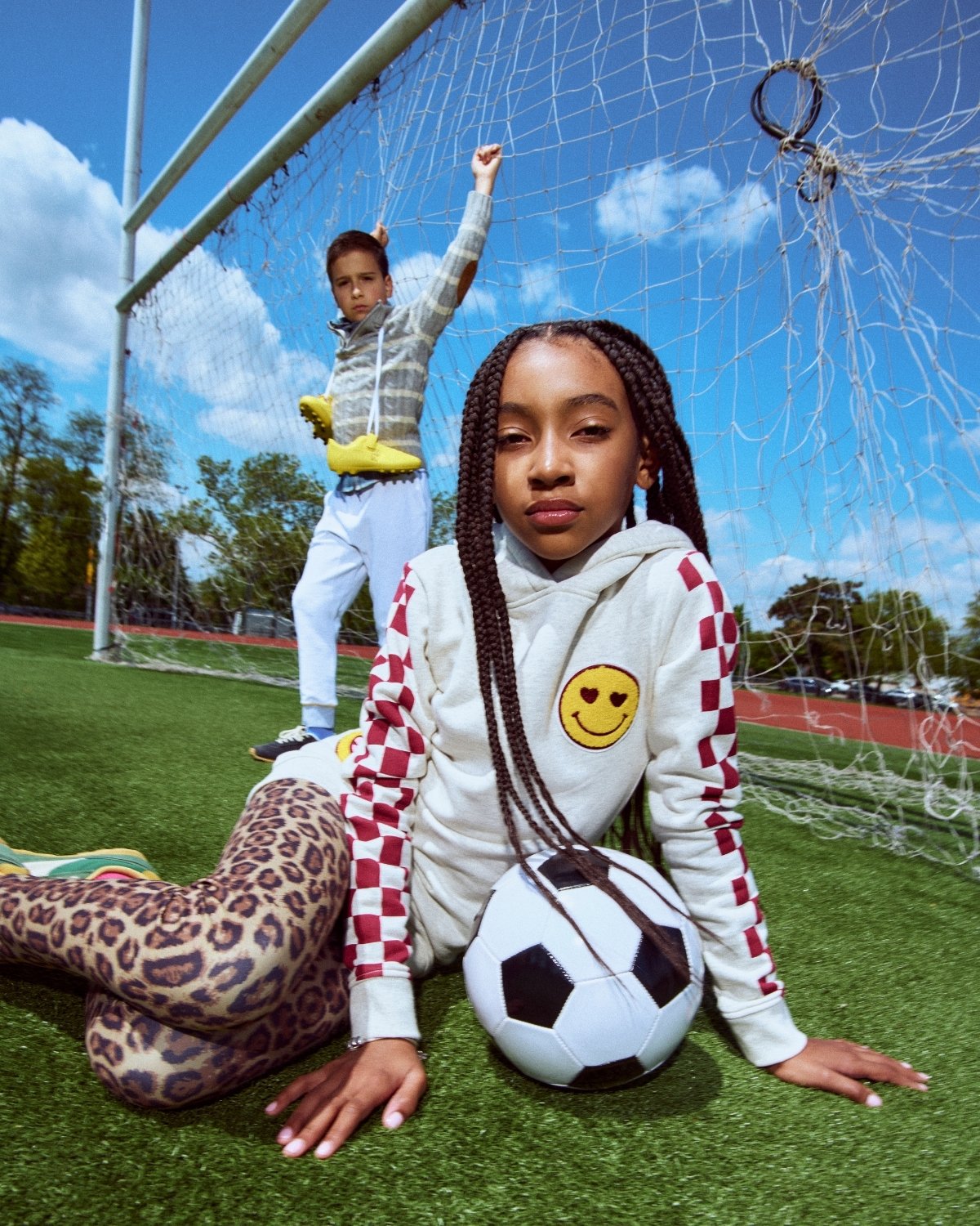 Two children on a soccer field with one holding a soccer ball.