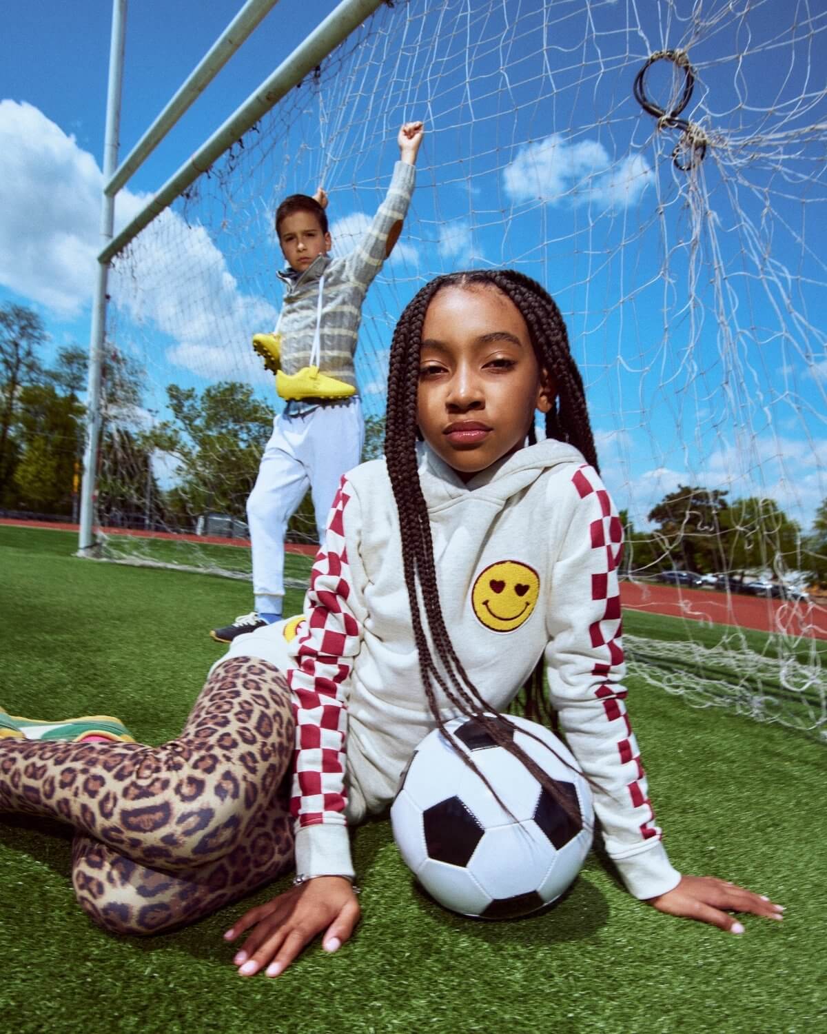 Two children on a soccer field with one holding a soccer ball.
