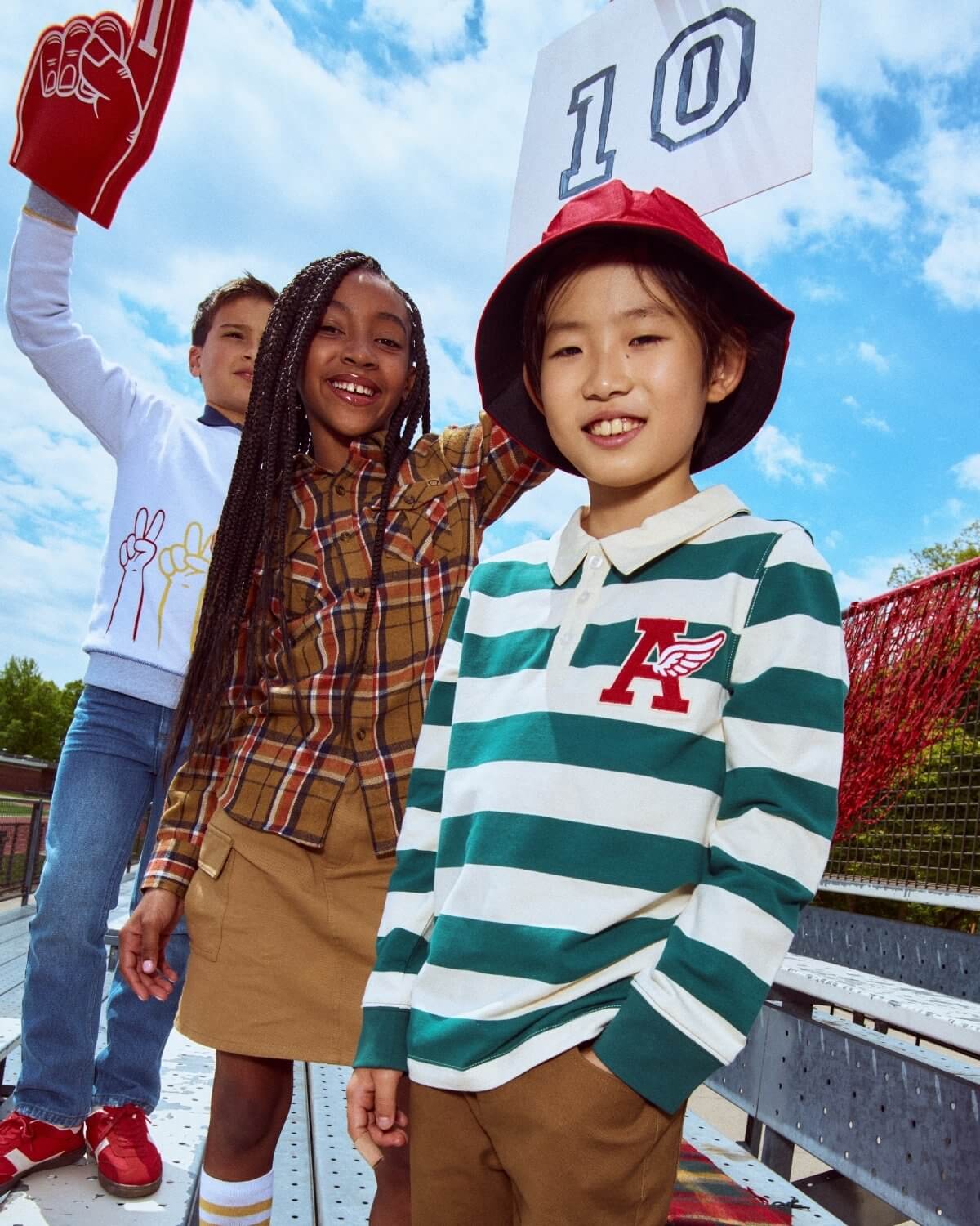 Three children standing on a bleacher with a clear blue sky in the background