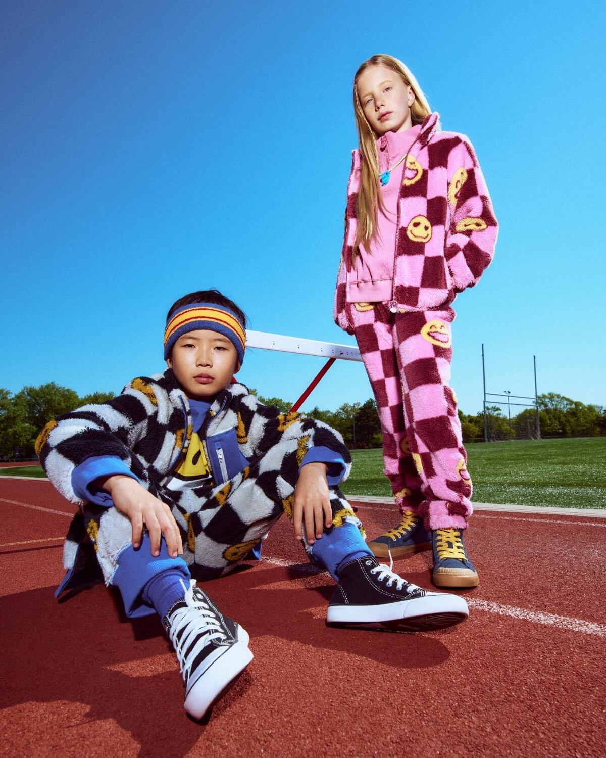 Two children in colorful outfits on a track field with a clear blue sky.
