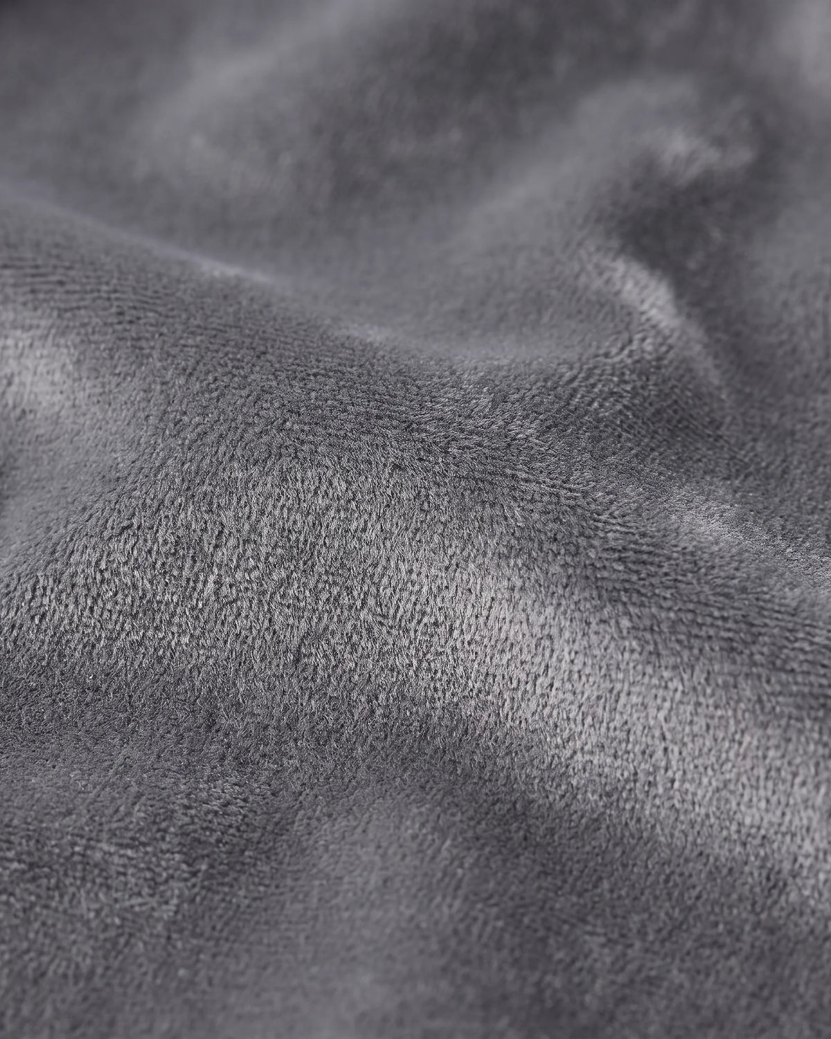 A close-up of a dark gray plush fabric texture with soft folds and a fine looped pile.