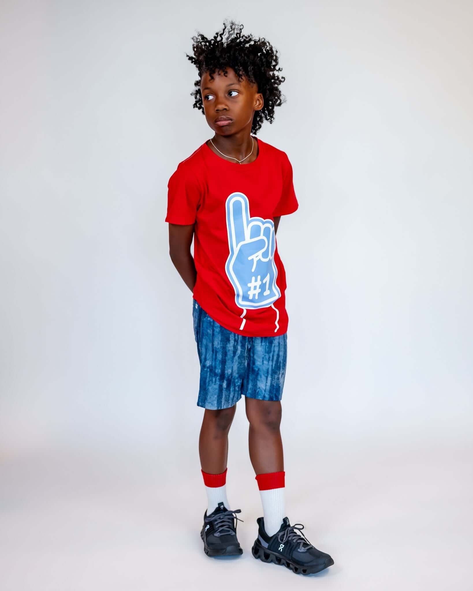 Child wearing a red t-shirt with a blue graphic and blue shorts on a white background