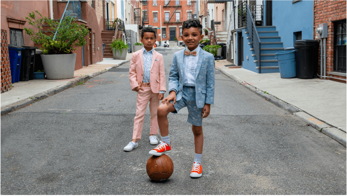 Two stylish boys in playful suits enjoying a fun day outside with a basketball, showcasing modern kids' fashion.
