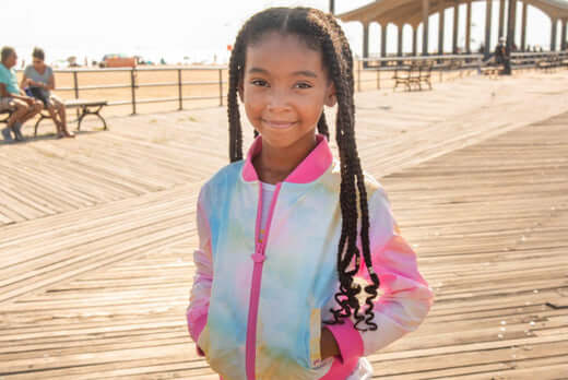 Stylish girl smiling in a vibrant tie-dye jacket, showcasing fun kids fashion for parents' style guides.