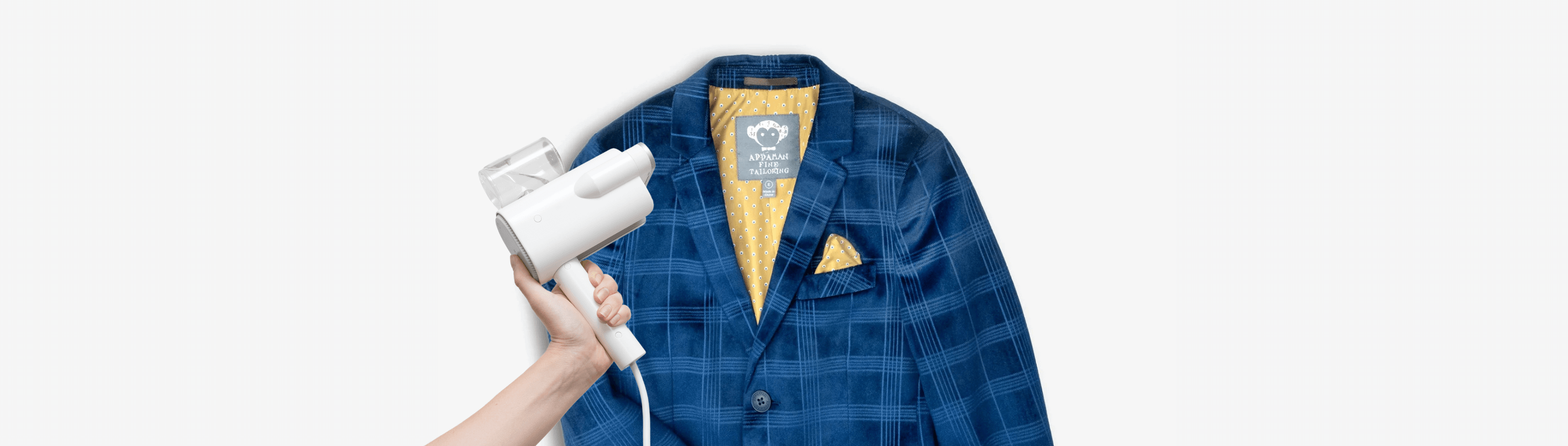 Hand holding a steamer over a stylish blue suit jacket, perfect for parents looking to freshen up kids' outfits.