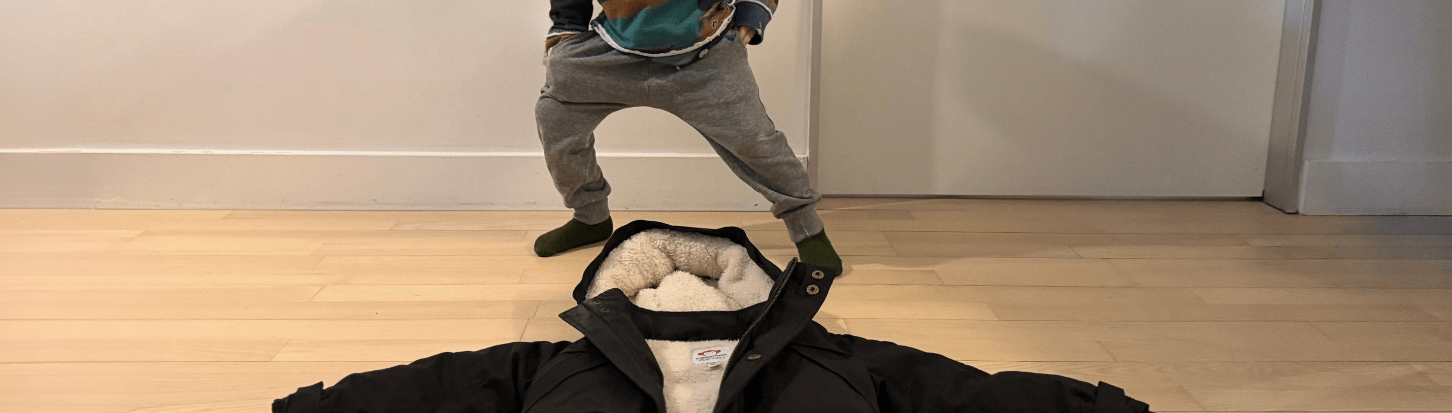 Toddler playfully refusing to wear a stylish winter coat, showcasing parent challenges in kids' winter styling.