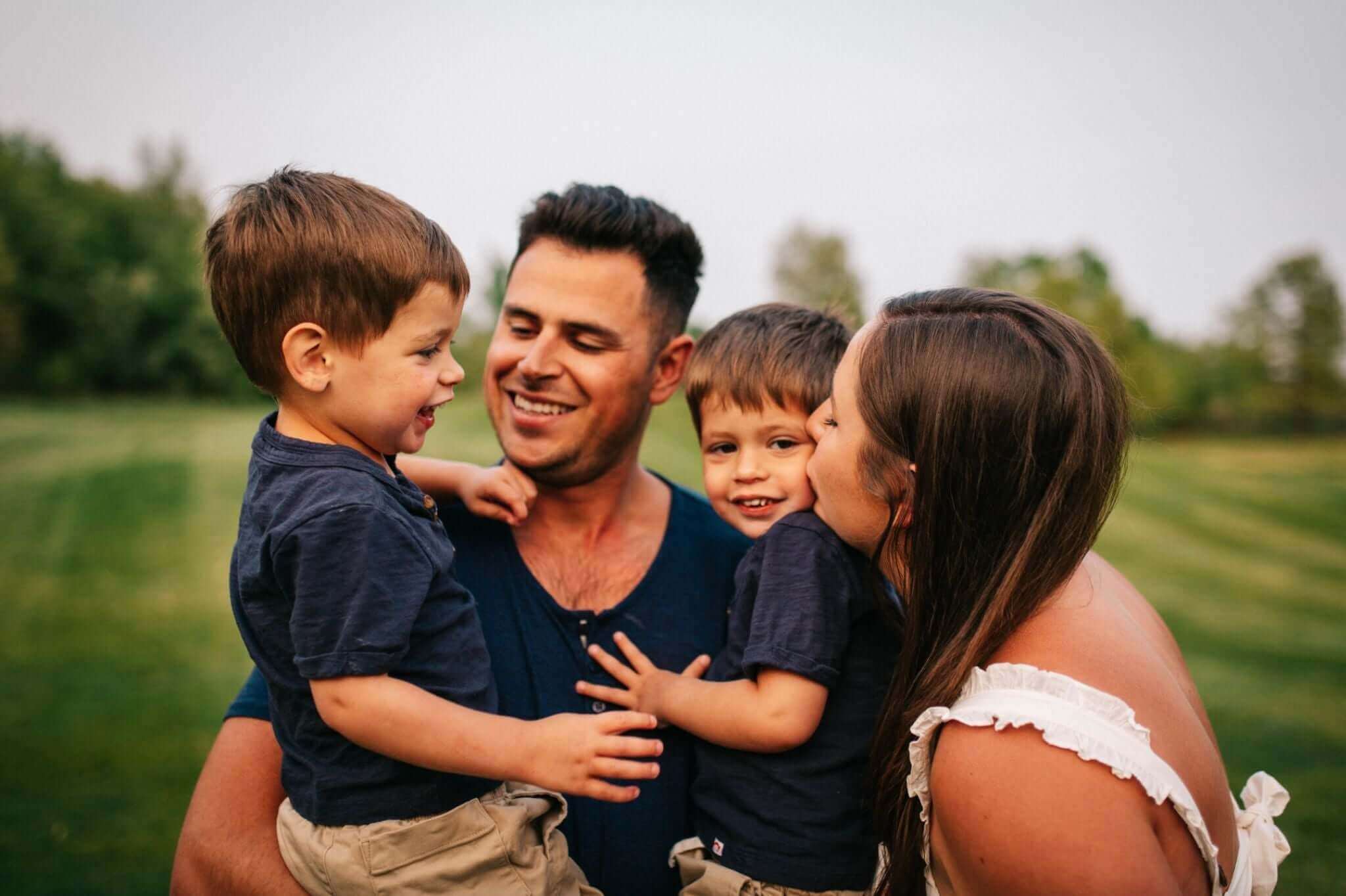 Joyful family moment with two boys in stylish outfits, captured in a lush outdoor setting.