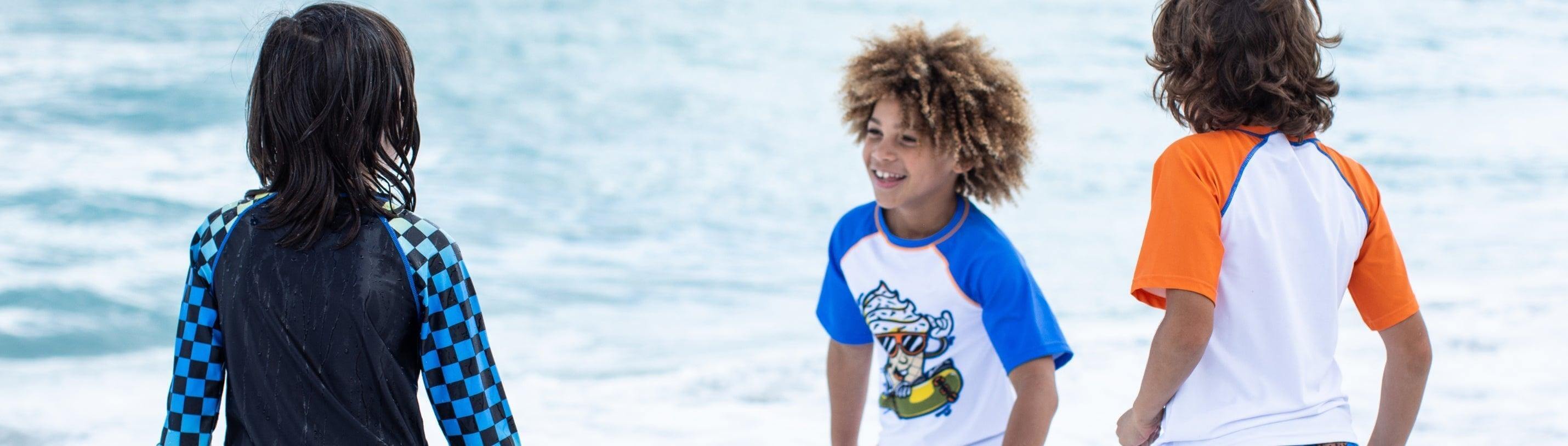 Three stylish kids in vibrant swim shirts enjoying a sunny day at the beach, embodying fun and safety in sun protection.