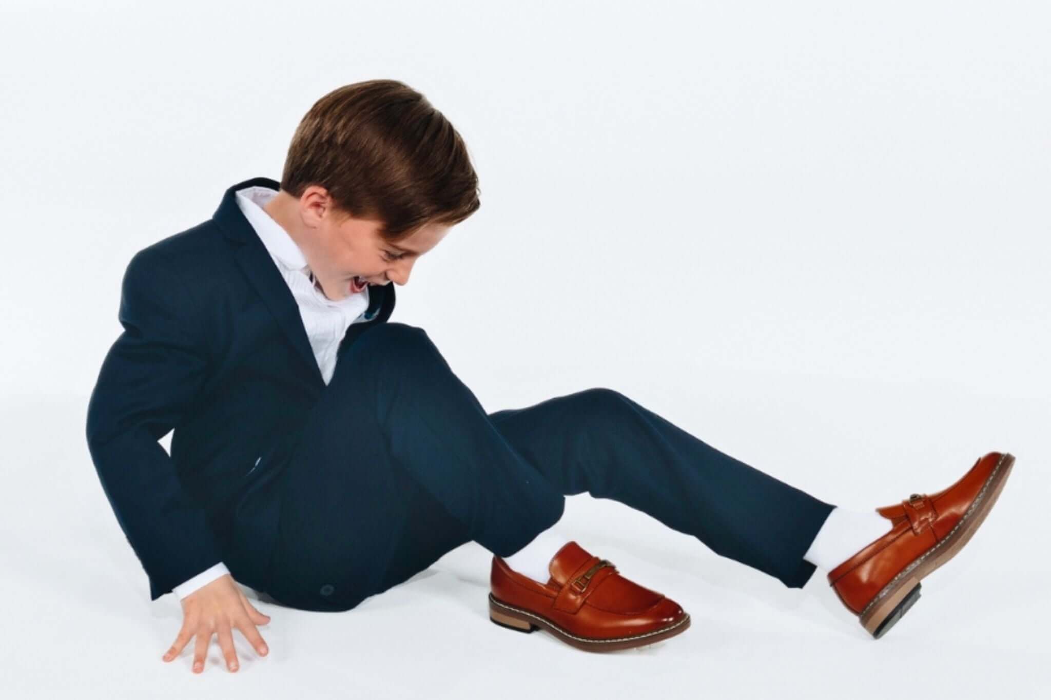 Stylish young boy in a tailored suit and smart shoes, showcasing playful Bar Mitzvah attire for modern kids.