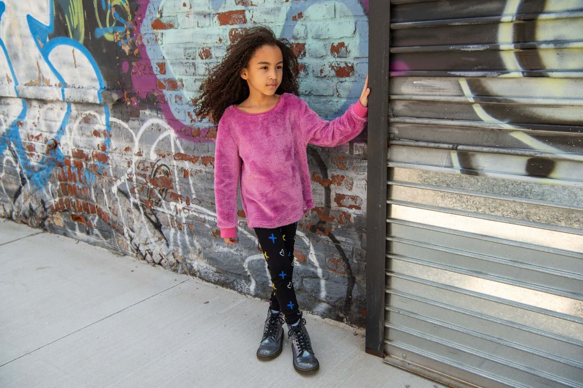 A stylish girl in a cozy purple sweater and star-patterned leggings, showcasing her unique style against vibrant graffiti.