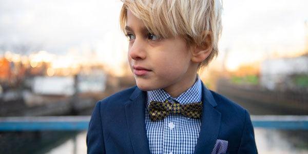 Stylish boy in a navy suit and patterned bow tie, showcasing modern kids' fashion with effortless charm.