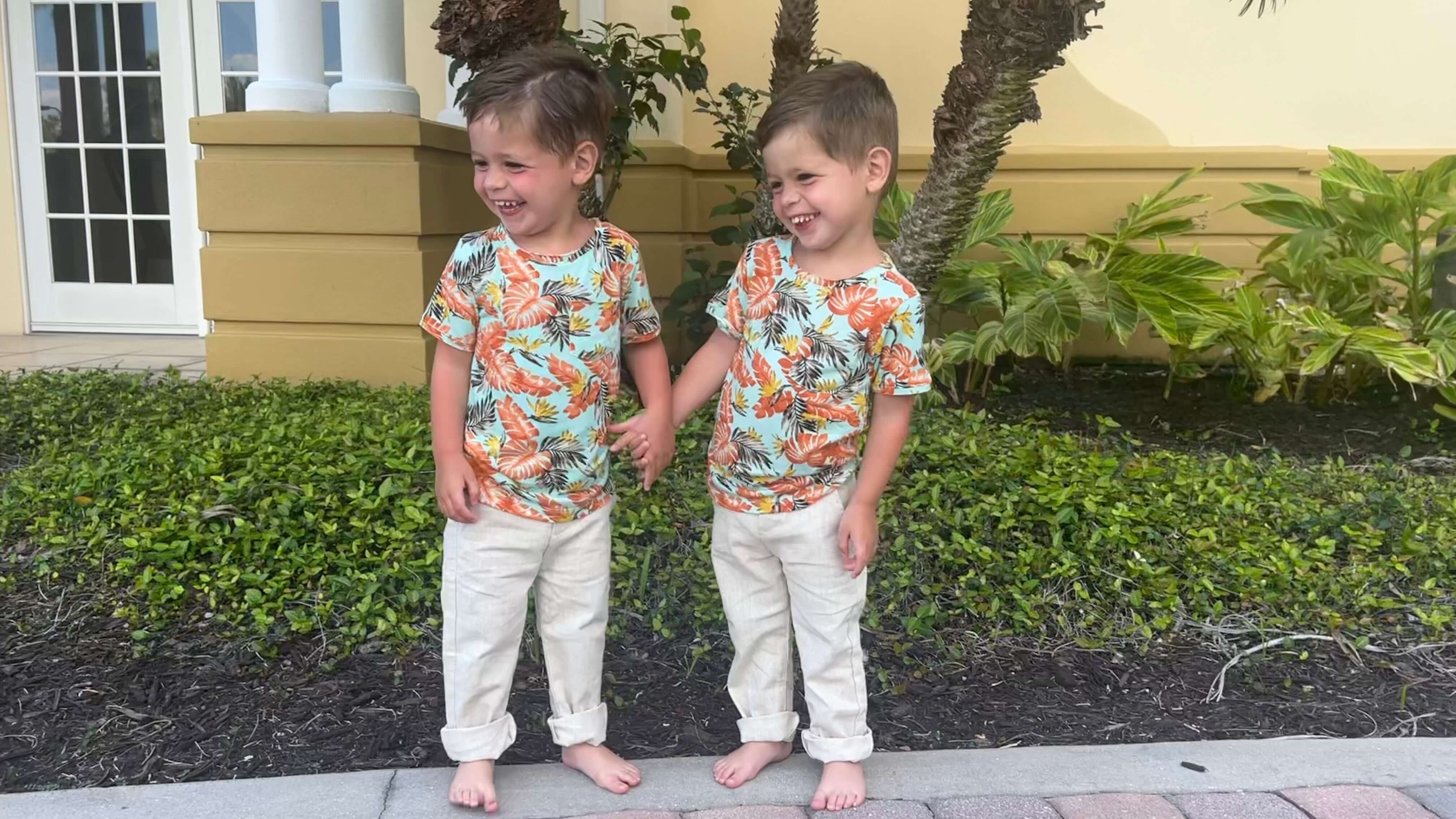Two adorable boys in matching tropical shirts and light pants, showcasing playful kids styling by Appaman.