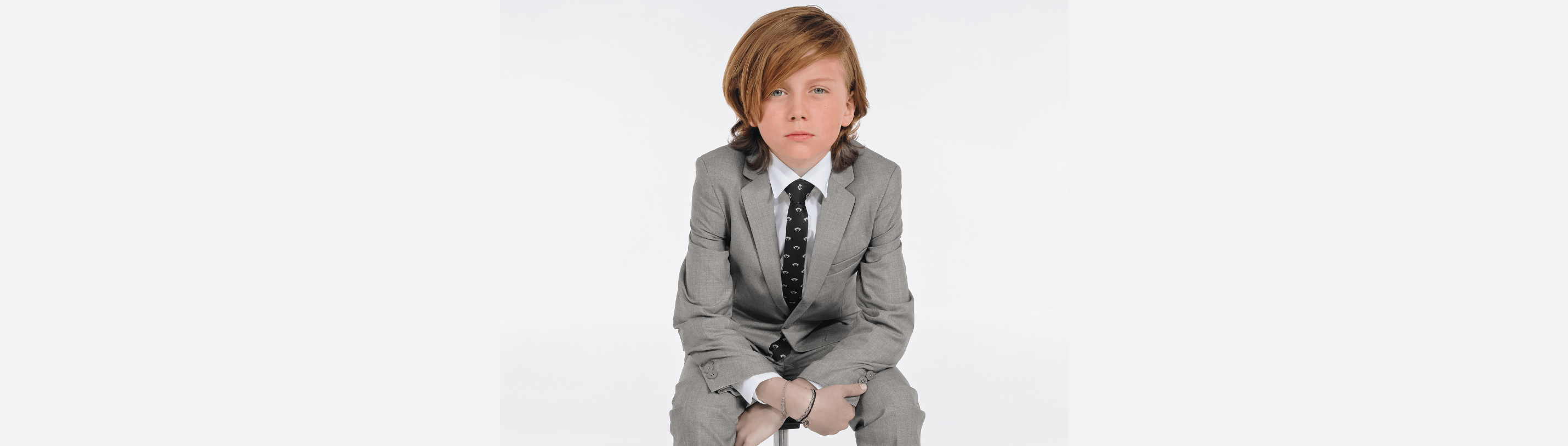 Stylish young boy in a sleek gray suit, exuding confidence with a playful vibe, perfect for dapper looks.