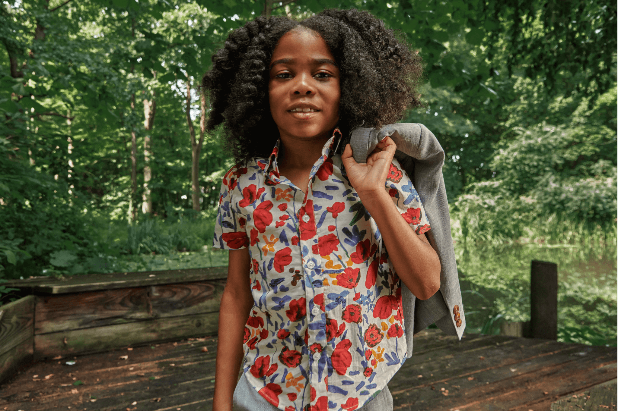 Stylish child in a vibrant floral shirt holding a blazer, showcasing playful eco-friendly fashion for kids.