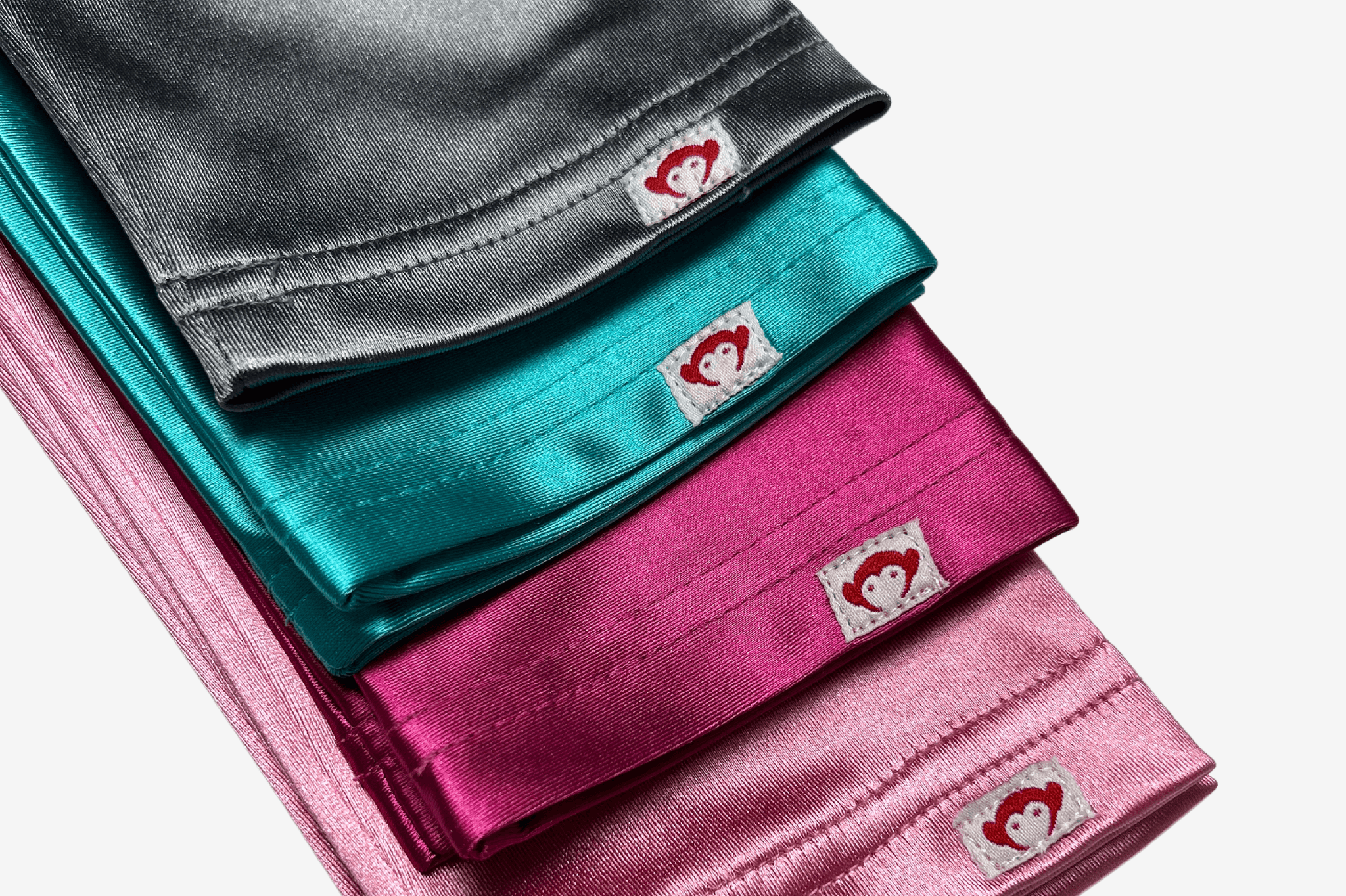 Colorful satin sleepover pillowcases in shades of grey, teal, pink, and fuchsia, featuring a playful heart logo.