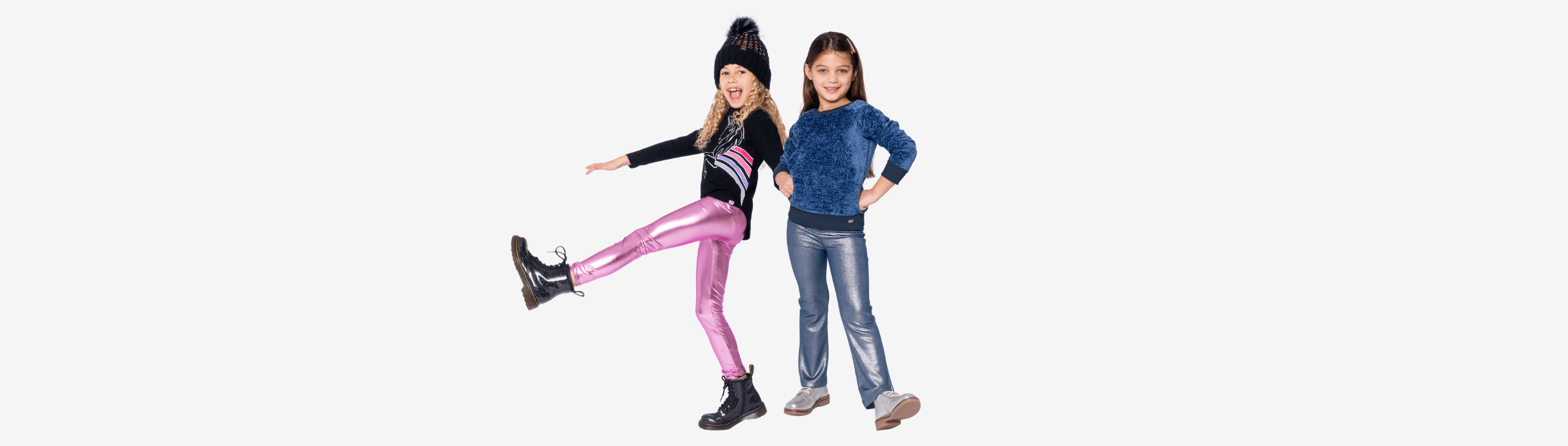 Two trendy girls showcase stylish outfits: one in shiny pink leggings and boots, the other in cozy blue top and jeans.
