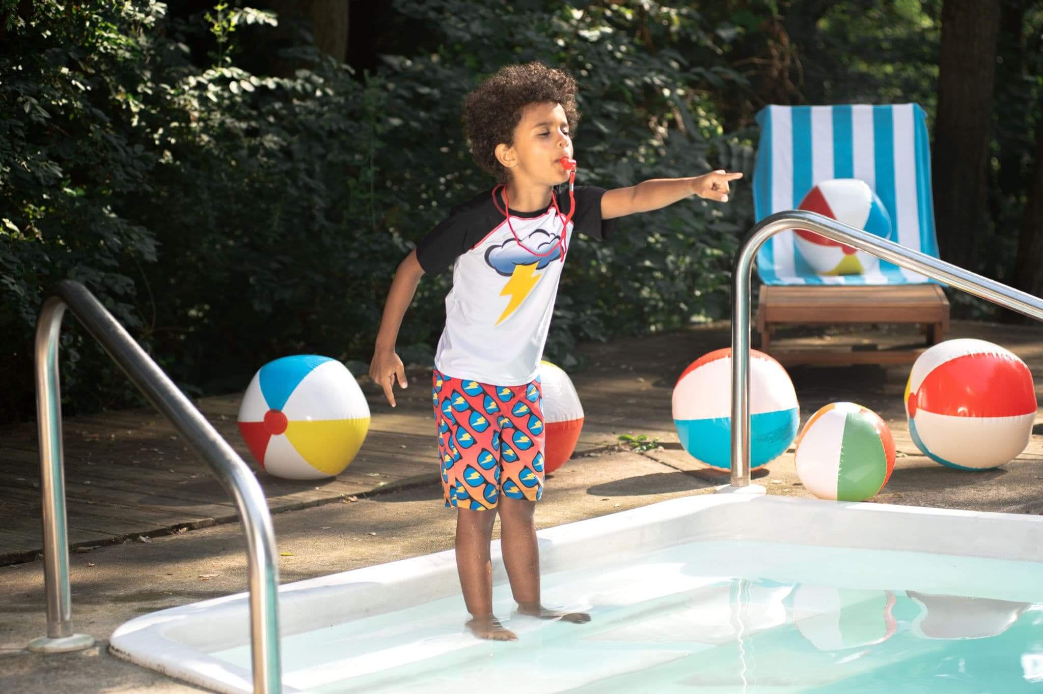 Stylish kid playfully ready to dive into the pool, wearing cool beach shorts and a playful tee, surrounded by colorful beach balls.