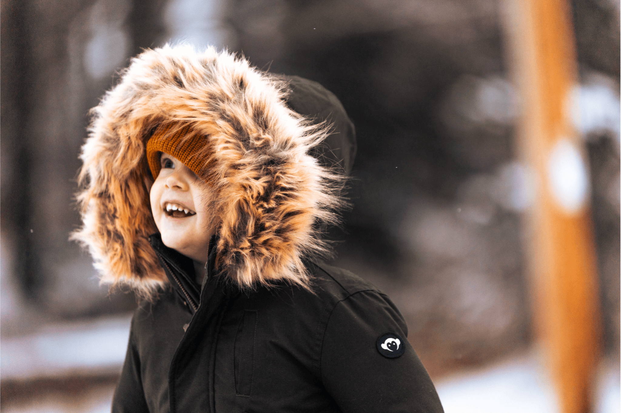 Stylish toddler in a cozy winter parka with a fur-lined hood, enjoying the snowy outdoors with a bright smile.
