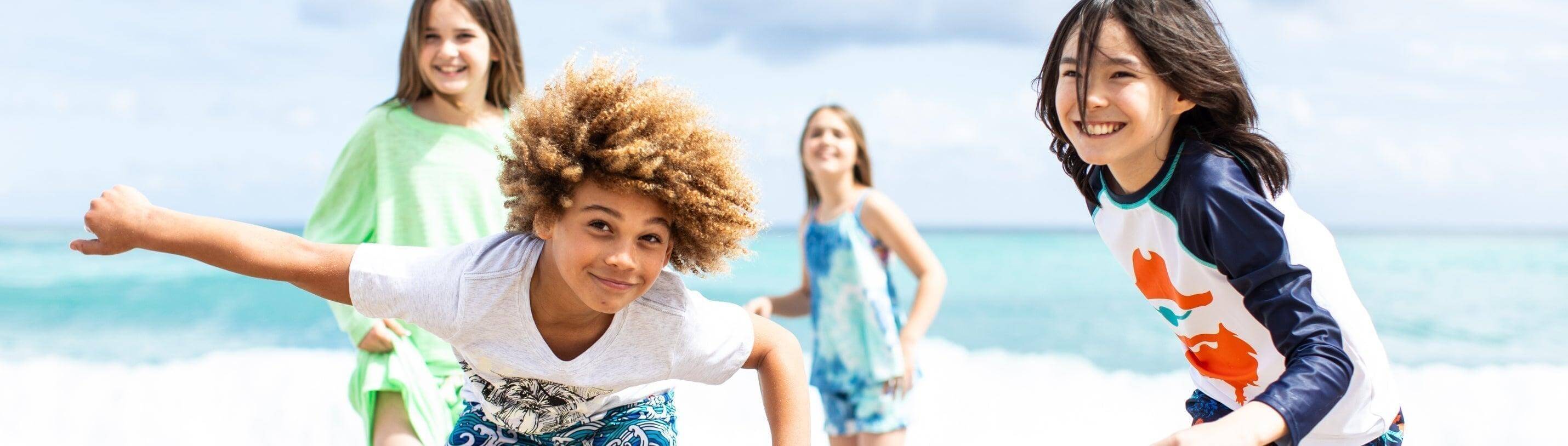 Four joyful kids playing on the beach in vibrant Appaman swimwear, ready for summer fun and adventure.