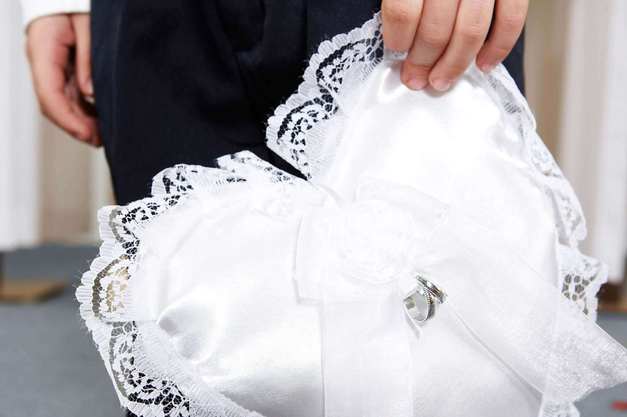 A stylish child holds a heart-shaped satin ring pillow adorned with lace, perfect for a wedding.