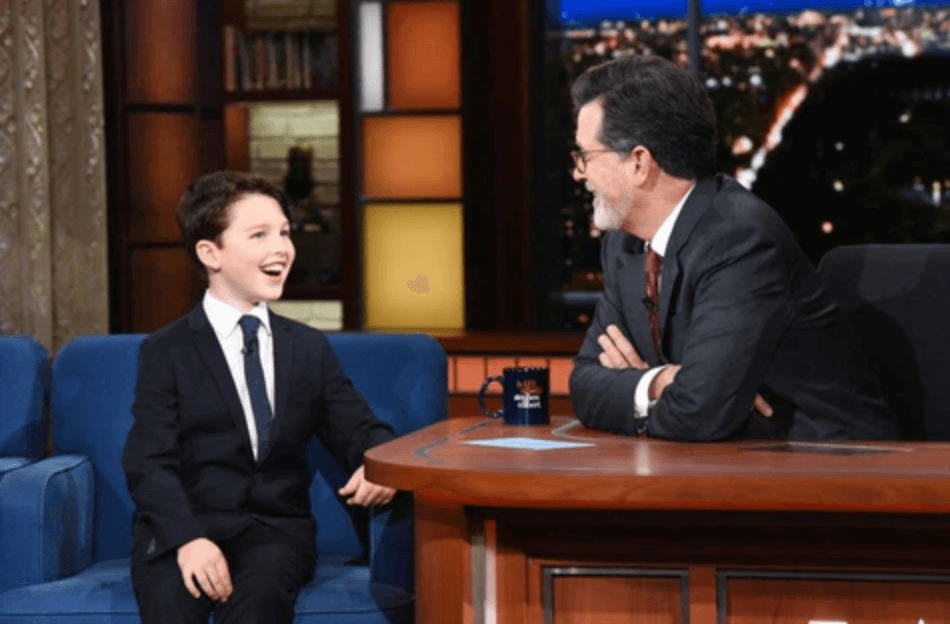 Young boy in a suit joyfully chatting with Stephen Colbert on a late-night talk show, showcasing stylish kids' fashion.