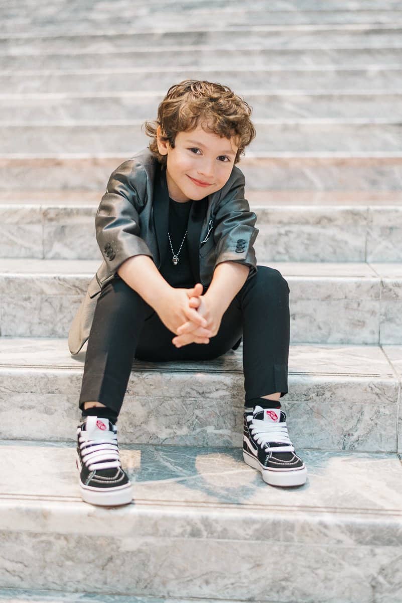 Cool kid in a silver tux jacket and black pants, showing effortless style with Vans sneakers—perfect for laid-back chic looks!