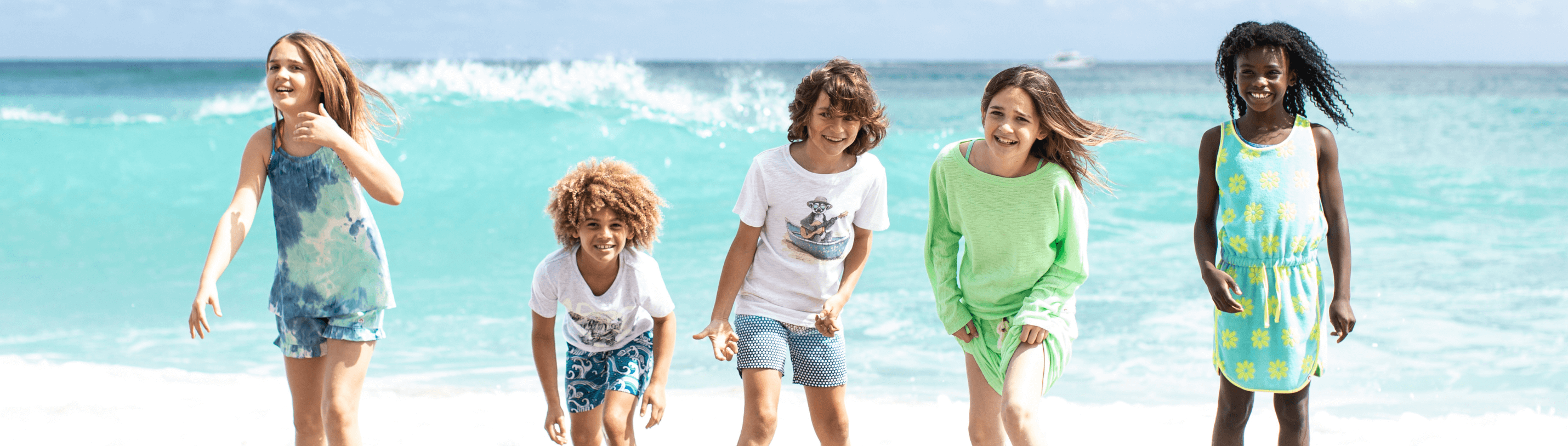 Five stylish kids in vibrant beachwear joyfully playing by the ocean, showcasing fun summer fashion for kids.
