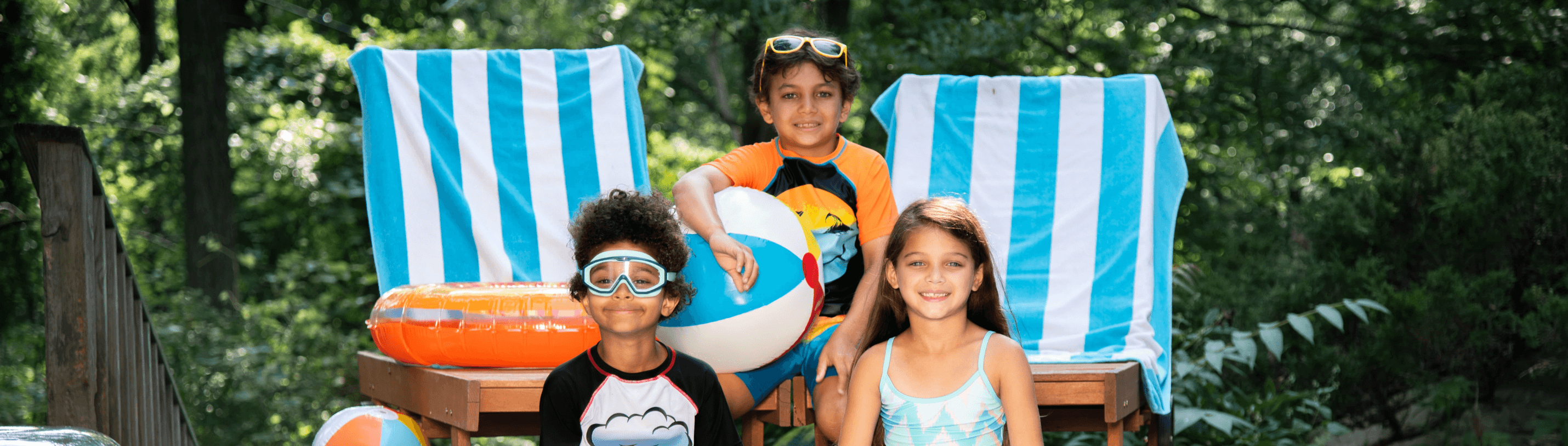 Three kids enjoying Memorial Day fun in stylish swimwear, relaxing on beach chairs with colorful pool toys.