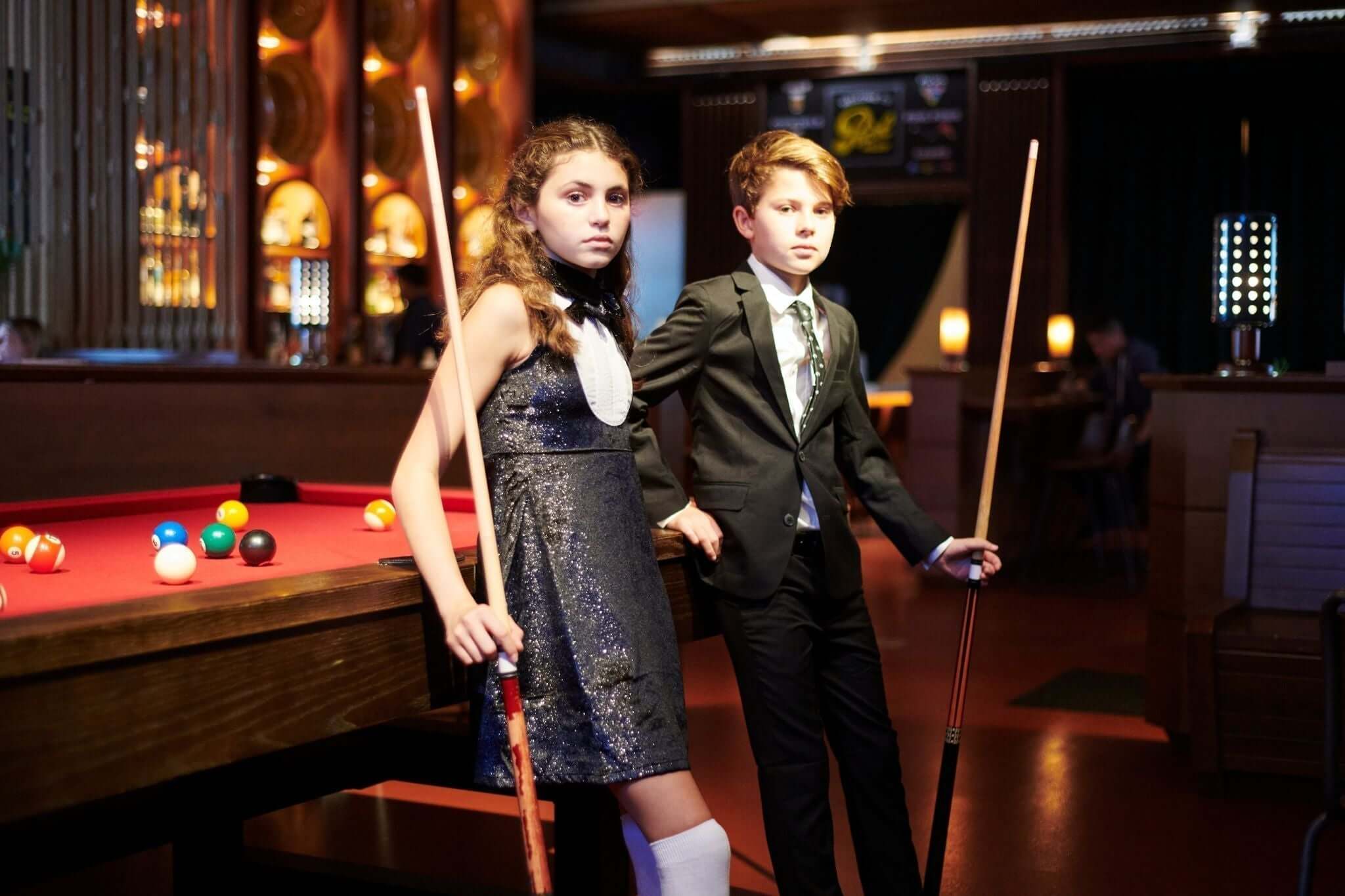 Stylish kids posing with pool cues, showcasing formal and semi-formal attire options for modern youth.