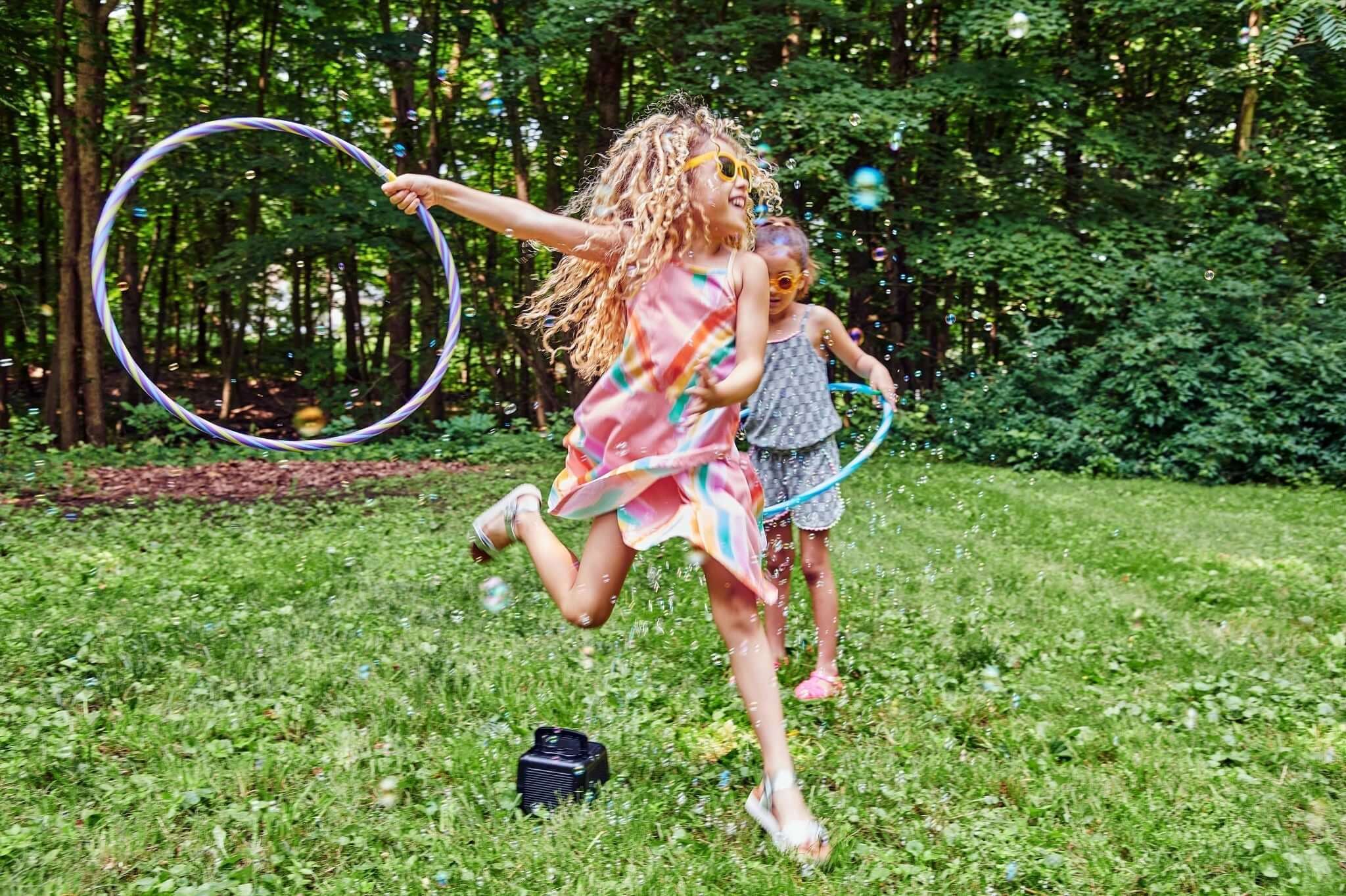 Two joyful girls playing with hula hoops in a vibrant green backyard, celebrating spring in stylish outfits.